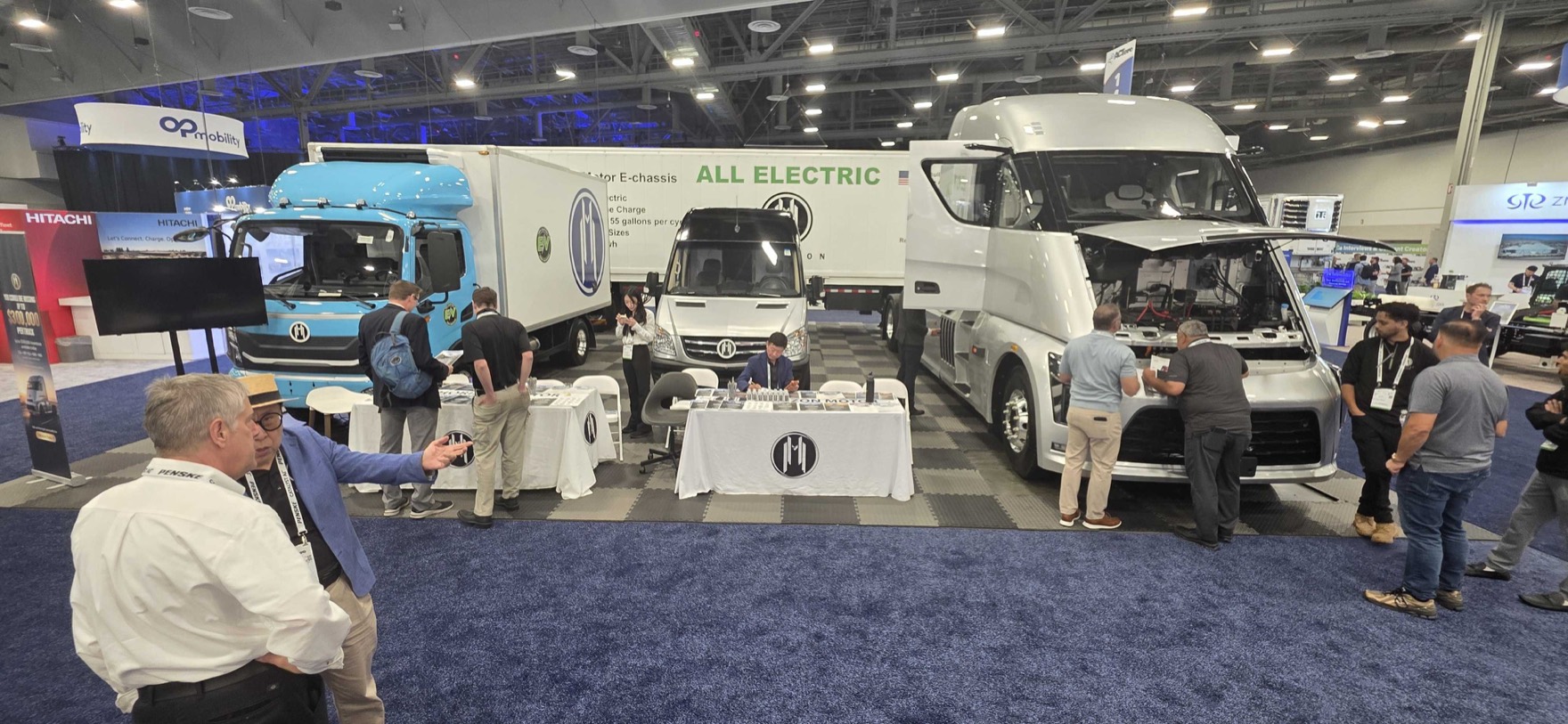 iMatrix at Horizon Motors Booth 1443, ACT Expo 2026 — three Horizon Motors all-electric trucks on display: a blue Class 8 cabover, a white E-chassis delivery van, and a white Class 8 sleeper tractor with hood open